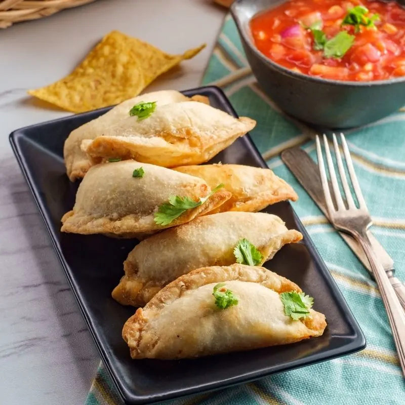 shrimp empanadas on a black plate, next there's a bowl of sauce.