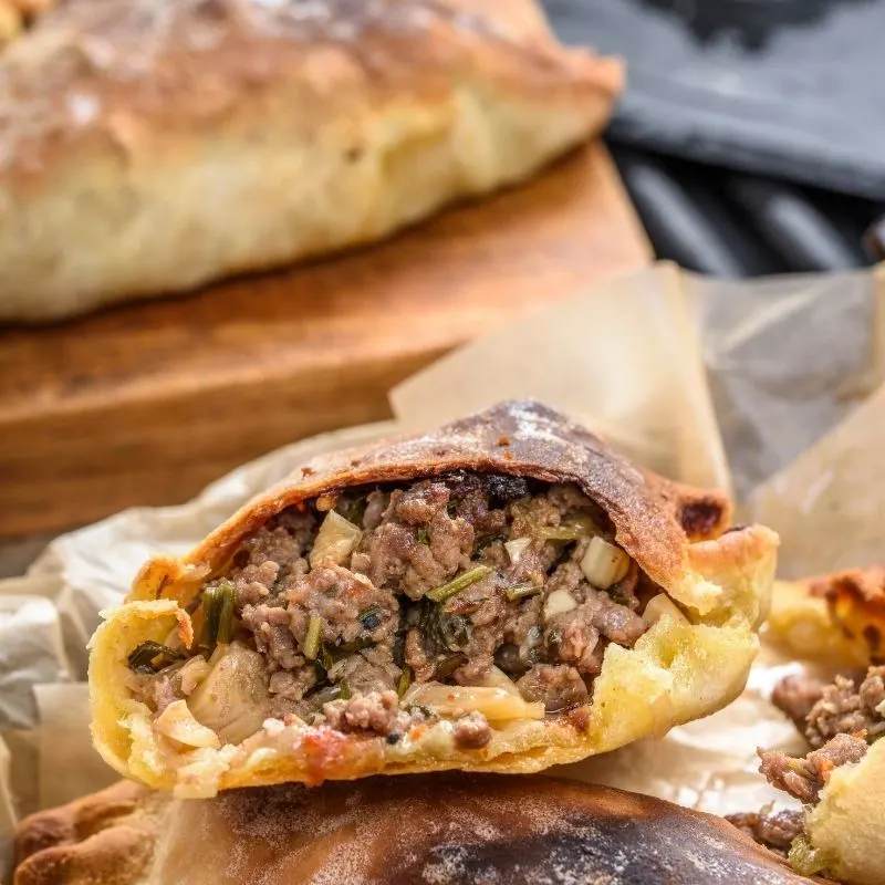 closeup with beef empanadas cut in half, with other empanadas in the background. 