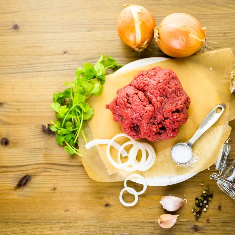 ground beef on a wooden table, with onions and seasoning for the spanish rice with ground beef recipe.