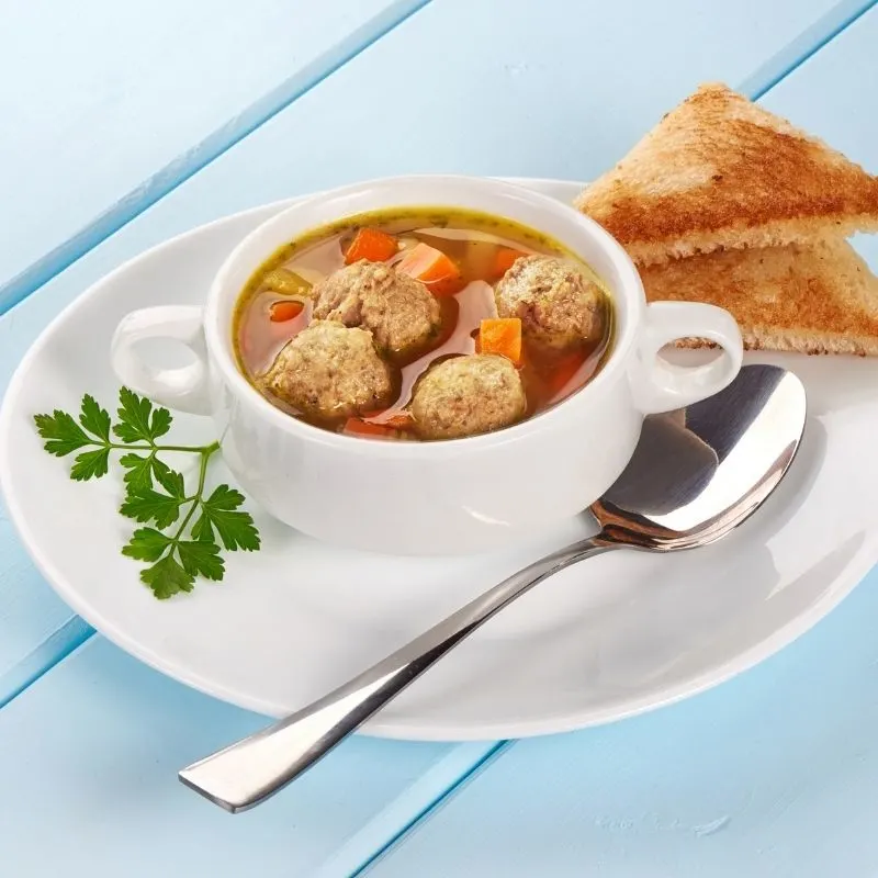 meatballs in a red soup on a bowl cup with spoon and triangular shaped bread