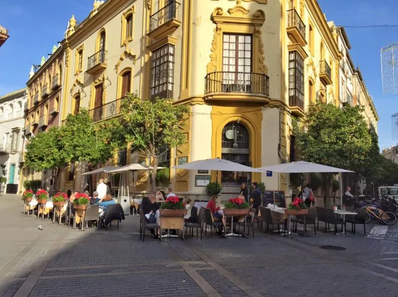 El Giraldillo, Seville - a restaurant on a yellow building with tables, umbrellas, chairs, and tables outside