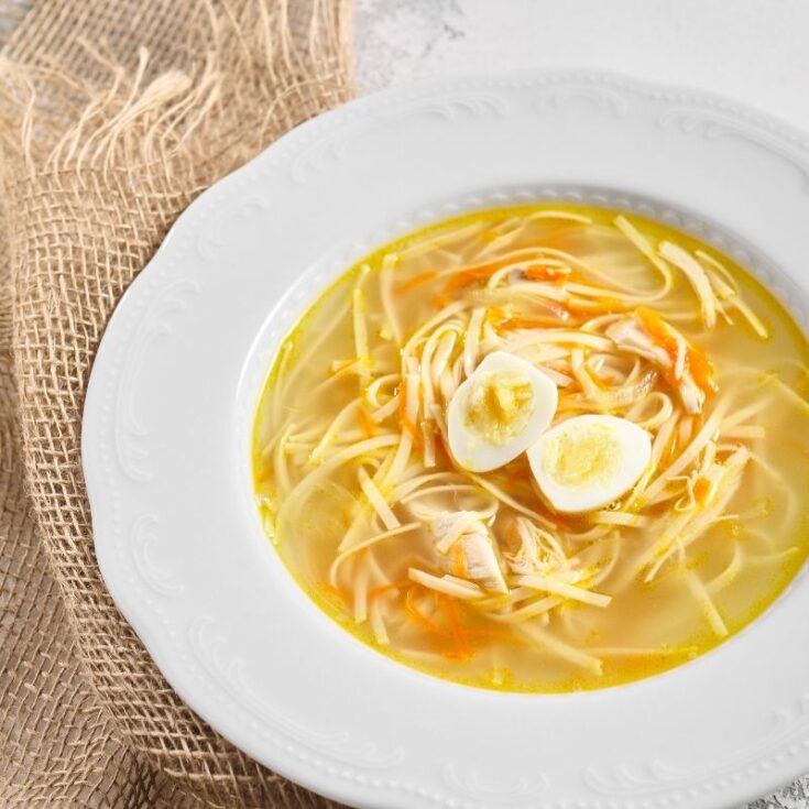 yellow soup served in a white bowl with pasta, , carrots, and topped with quail eggs
