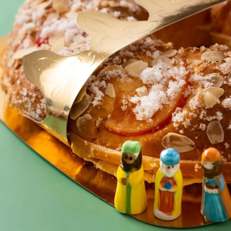 a closeup of a christmas cake being sliced with three king figurines on the side