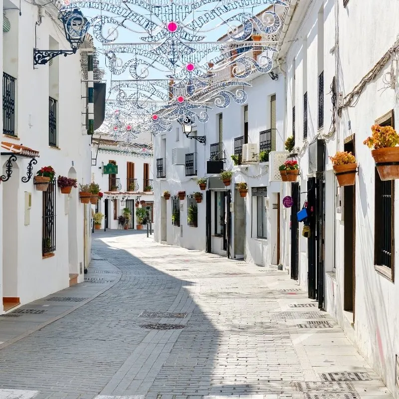 Christmas decorations on top of the street in the middle of row of white houses - The International Christmas Fair in La Cala de Mijas