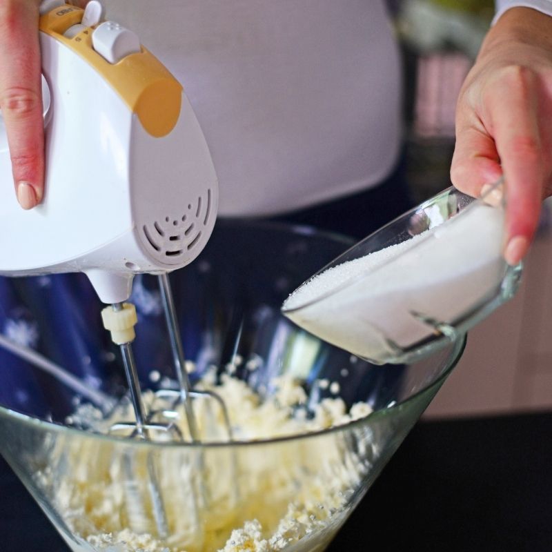 A woman using a hand mixer to mix butter and sugar in a glass bowl for the pumpkin flan recipe