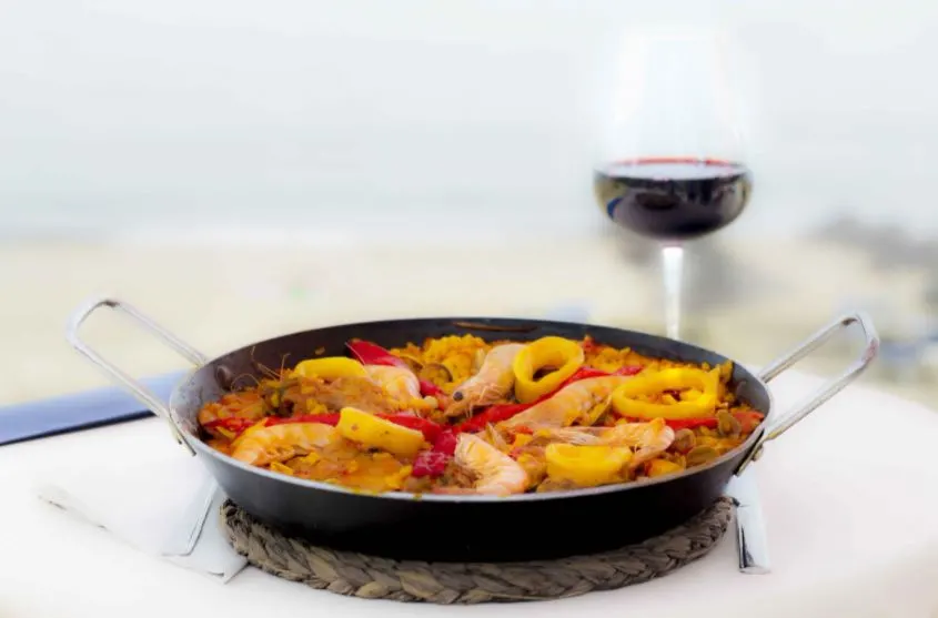 Paella in a pan and a glass of red wine served at Chiringuito El Cachalote