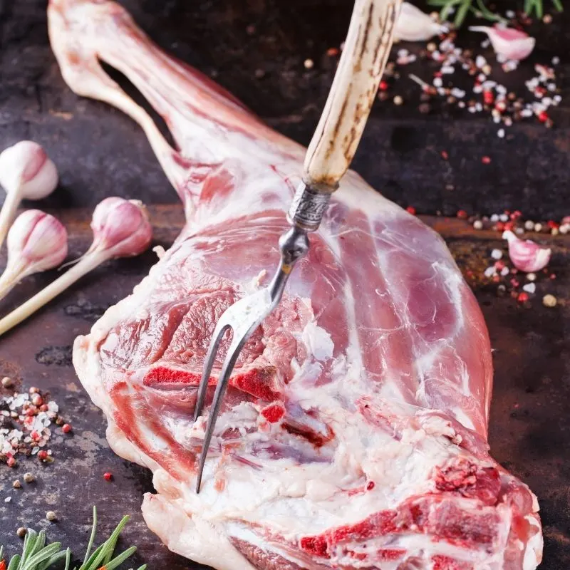 a whole lamb leg on a table with garlic next to it.