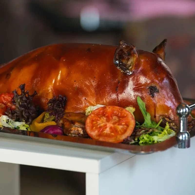 closeup of a roasted suckling pig on a brown tray with vegetables in a restaurants