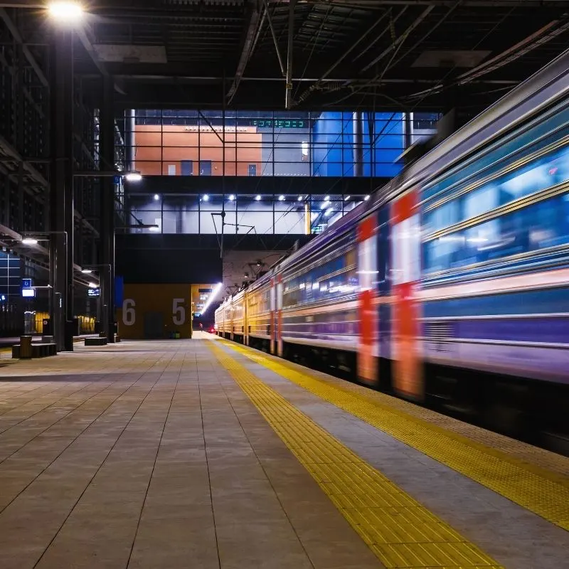 Moving train in a train station and on the background there's travel information on a screen.