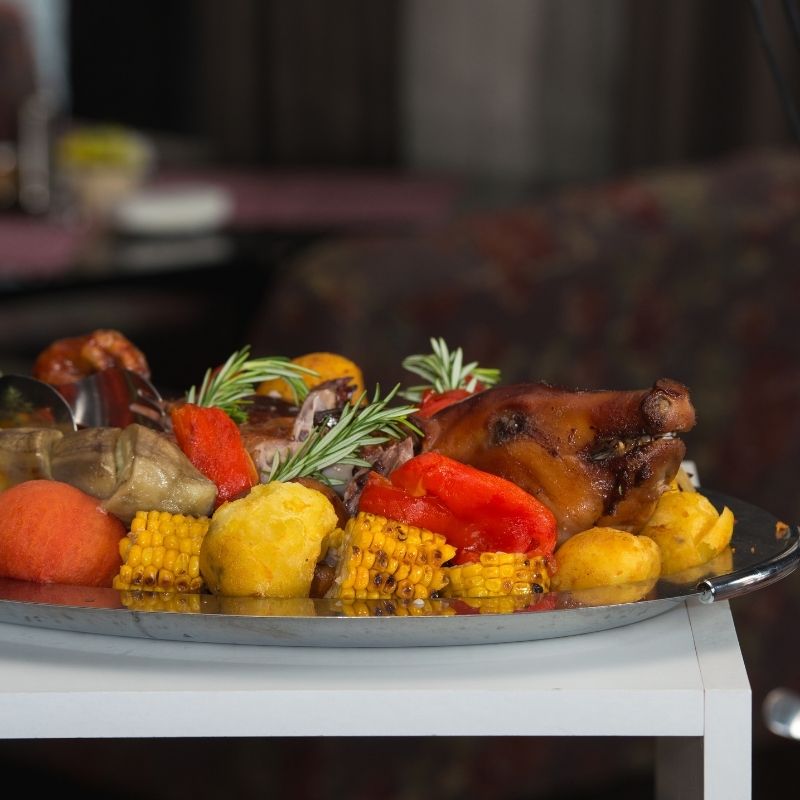 a closeup of a whole roasted pig on a plate with corn, vegetables, and the background is a living room