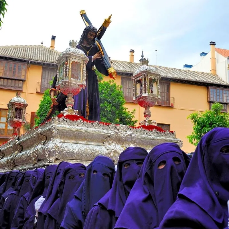 a statue of jesus carrying the cross being carried by devotees dressed in robes 