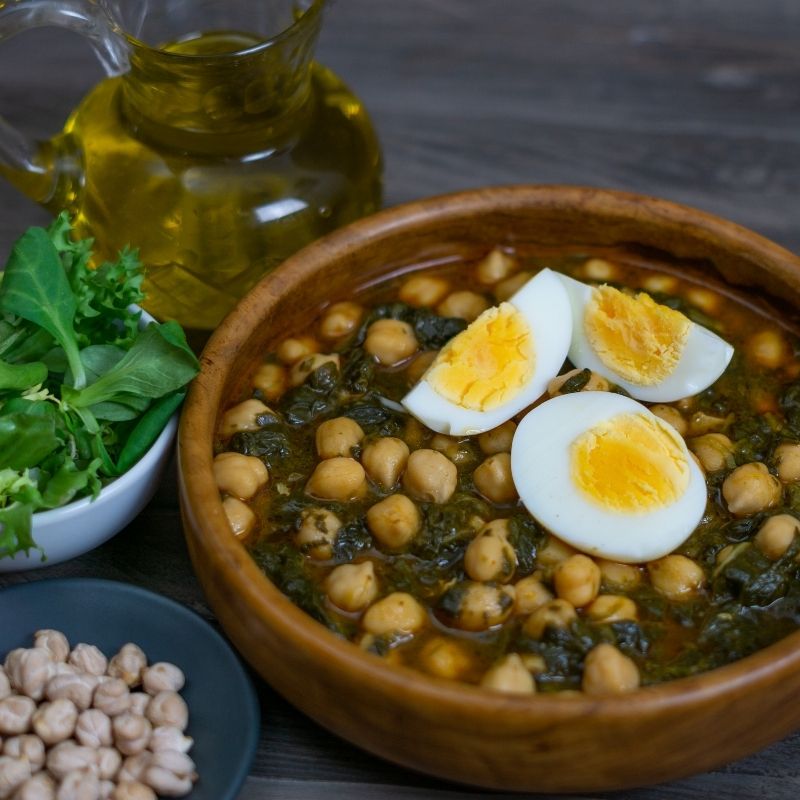 chickpea and spinach stew in a clay bowl served with boiled egg.