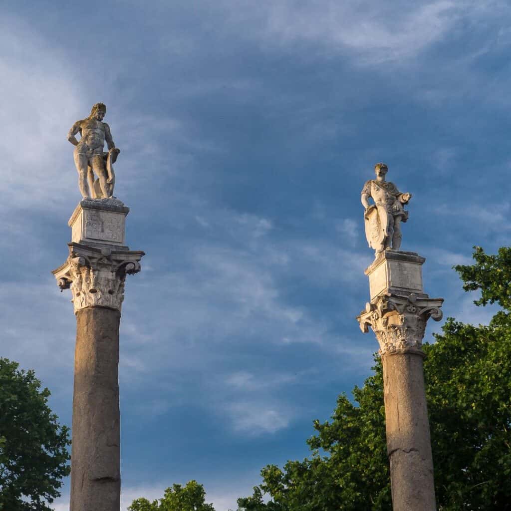 two statues on top of columns with trees in the background
