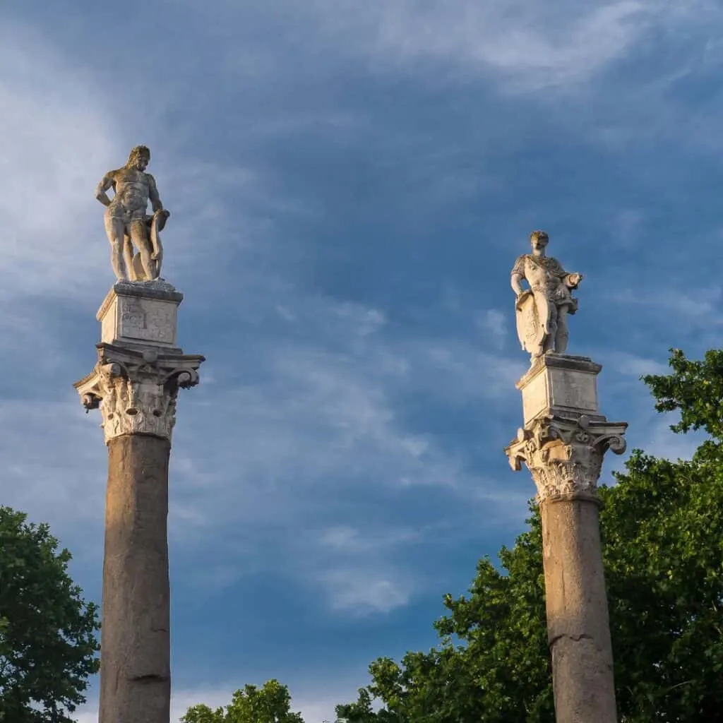 two statues on top of columns with trees in the background