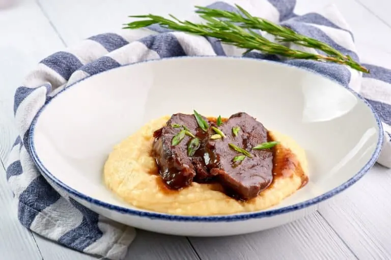 Braised pork cheeks dish on a white plate served with mashed potato on a wooden table. Tender Braised Pork Cheeks from Spain.