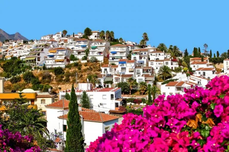 aerial view of Nerja, filled with white houses and orange roofs and pink Bougainvillea flowers on the forefront