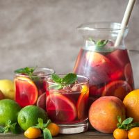 sangria in a jar surrounded by fruits like oranges, limes and peaches.