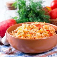 Spanish vegan rice in a clay bowl with vegetables in the background.