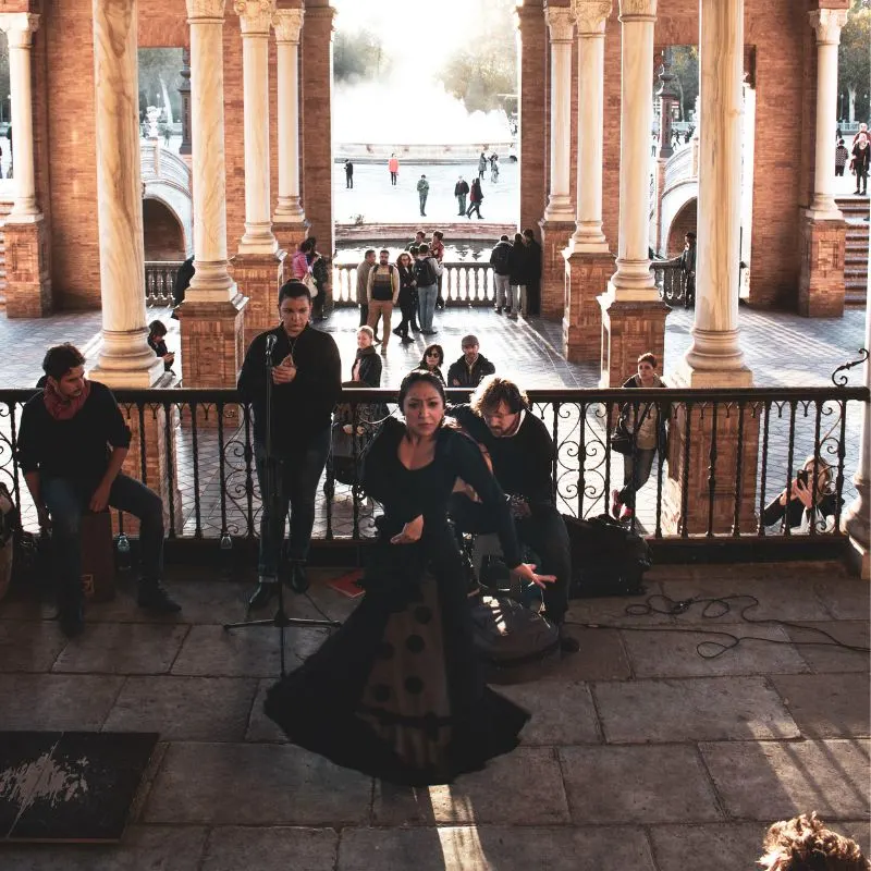 a woman in black dancing flamenco with musicians at the back on an old building