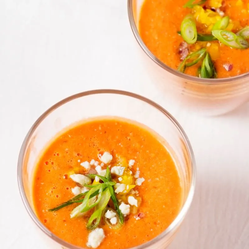 carrot gazpacho in 2 bowl on a white surface.