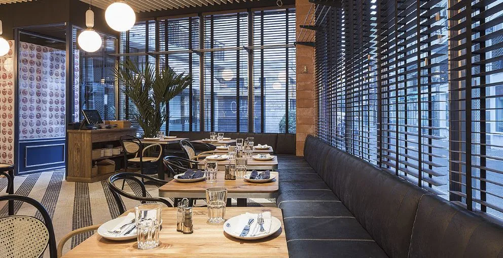 Castizo, a restaurant with windows and on a living room with a wooden table and with plates