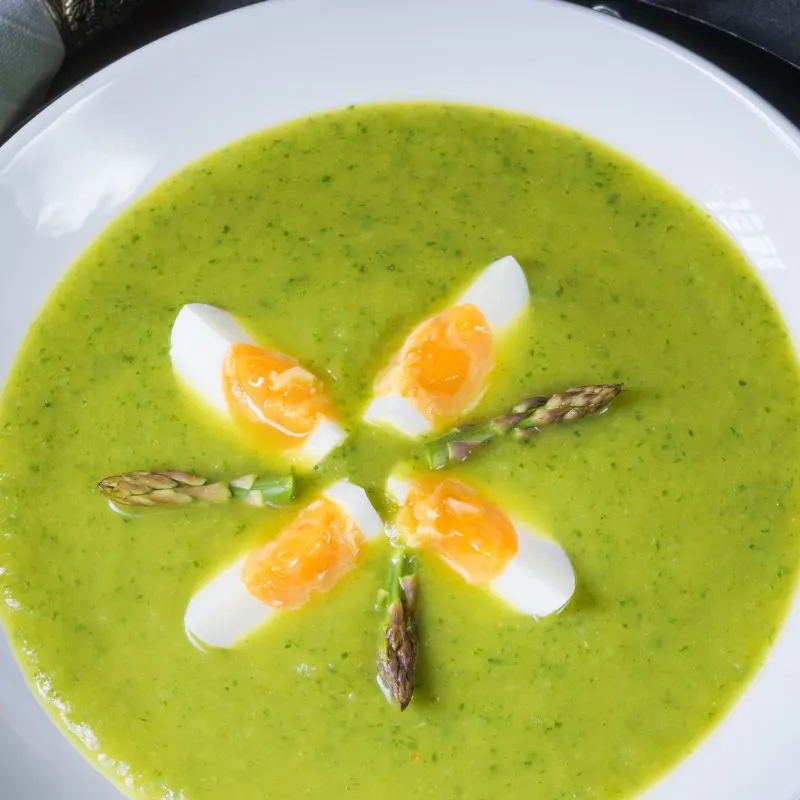 cold asparagus soup in a bowl with boiled egg on top and small pieces of asparagus. 