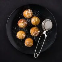 fried fritters on a black plate, dusted with powdered sugar