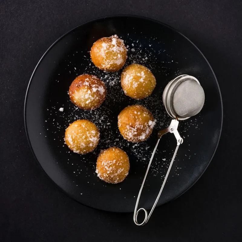 fried fritters on a black plate dusted with powdered sugar