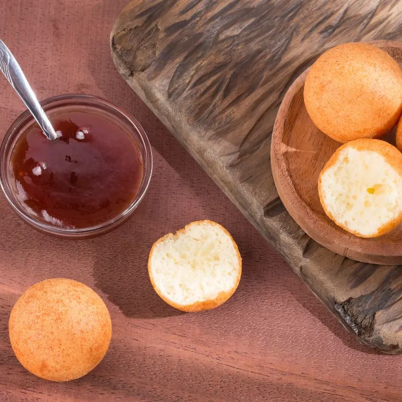 Buñuelos on a wooden plate next to a small bowl of fruit jam