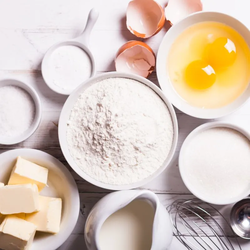 baking ingredients for dulce de leche cupcakes such as 2 eggs, white flour, white sugar and cubes of butter in bowl