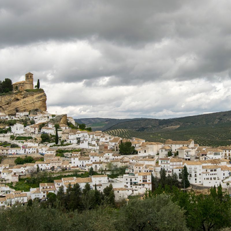 landscape view of Montefrío in Granada filled with white houses on the mountain and a church tower on the upper side of the hill with dark clouds