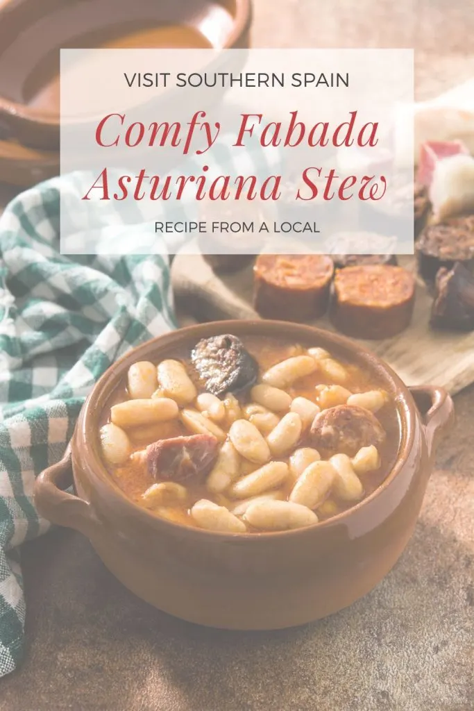 A photo with a bowl of Spanish bean stew on a wooden table next to ingredients for the stew. On top of the photo it's written comfy fabada asturiana stew.