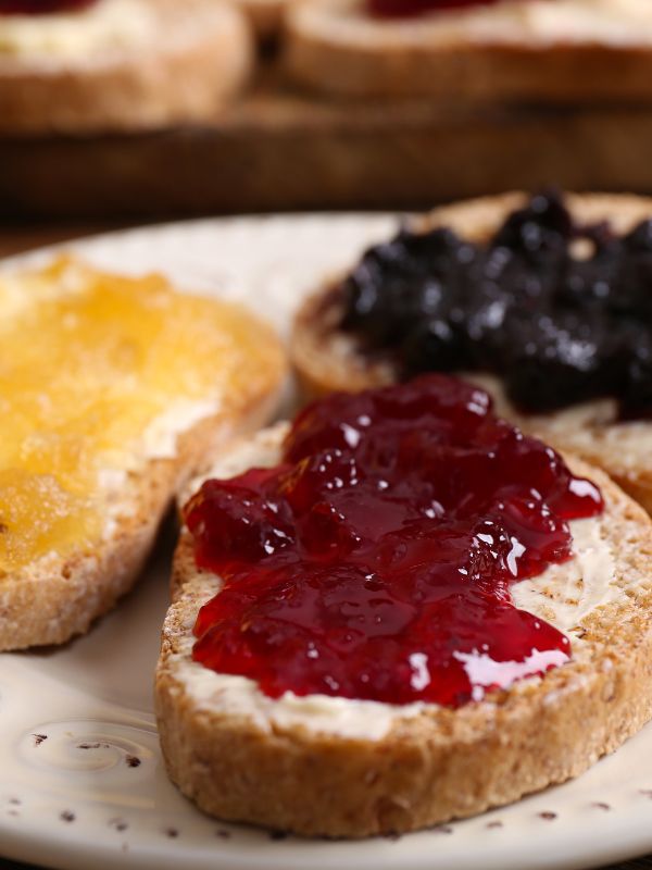 3 different spanish toasts with butter and jam on a white plate.