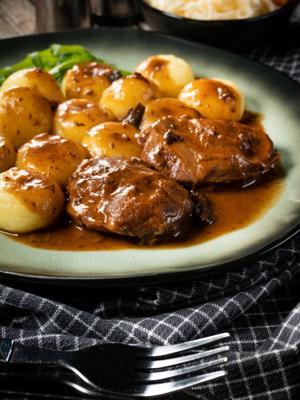 Carrilladas de Cerdo with boiled potatoes and gravy on a white plate.