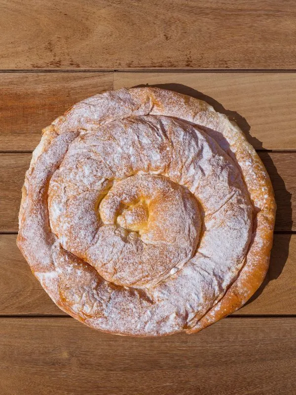 Ensaimada dusted with powdered sugar on a wooden table