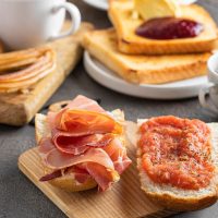 Spanish breakfast foods such as tomato toast, jamon, churros, coffee on a dark surface.