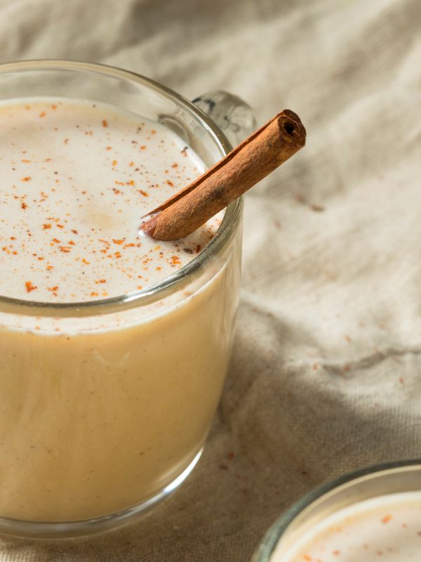 a glass of coquito recipe decorated with a cinnamon stick on a white table cloth.