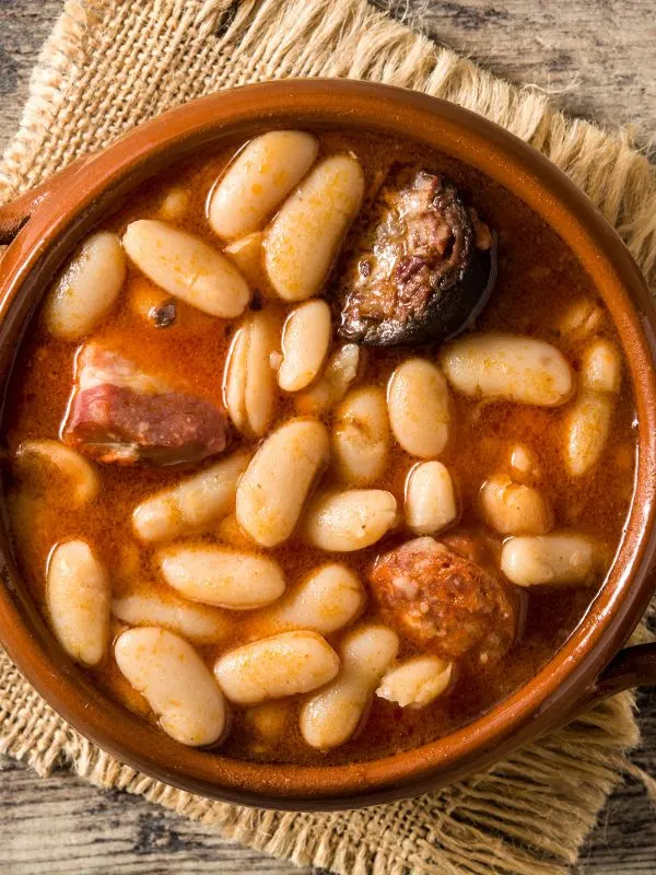 asturian bean stew in a clay bowl on a wooden table. 