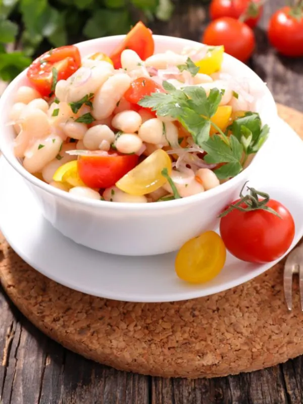 a white bean salad on a bowl on a saucer with tomatoes on the saucer and table