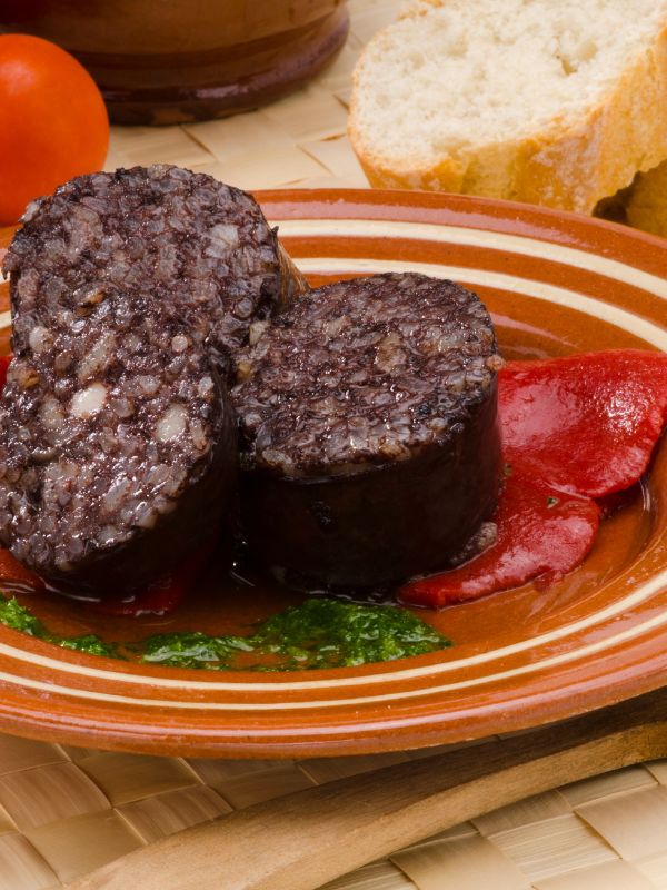 black pudding on a clay plate, served with bread and tomato.