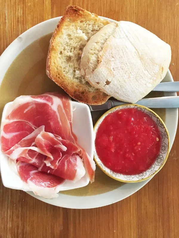 Pitufo bread, jamon on a white plate next to a bowl of red sauce.