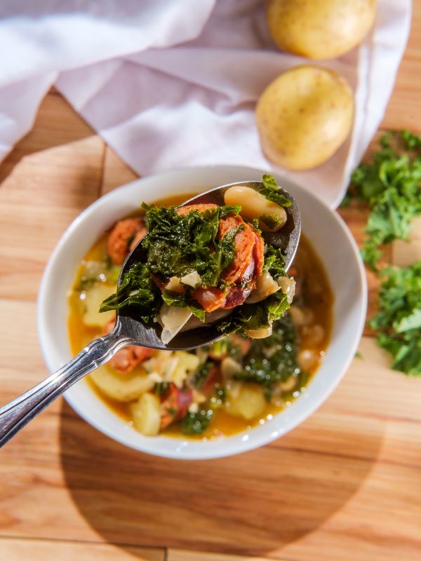 caldo gallego soup from spain in a white bowl on a wooden table and a closeup with a spoon full of caldo soup.