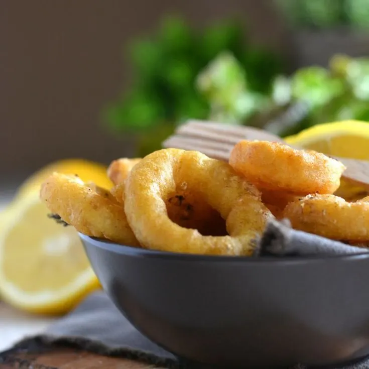 closeup with fried calamari rings in a gray bowl and in the background there's a slice of lemon