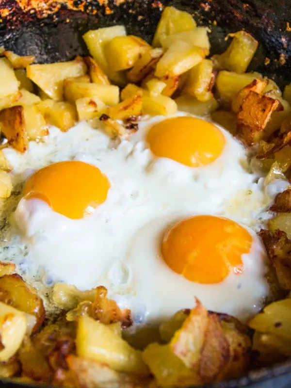 closeup with spanish fried potatoes with 3 fried eggs in iron pan