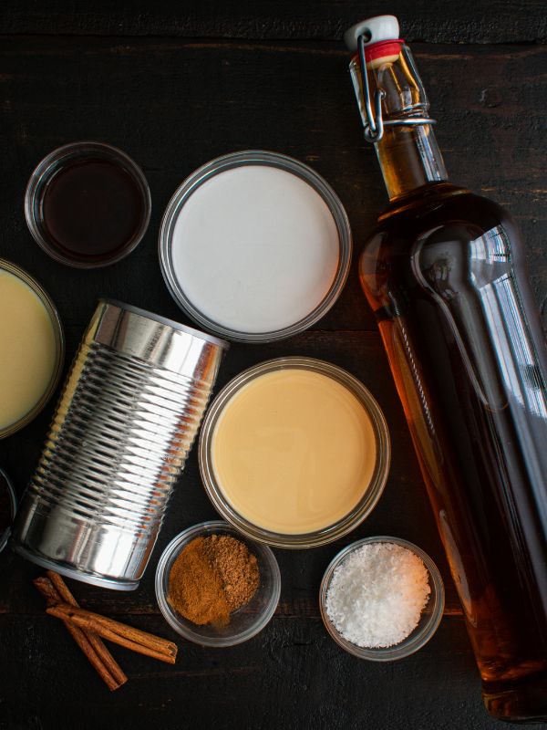 coquito ingredients such as rum, condensed milk, cinnamon, evaporated milk on a wooden table