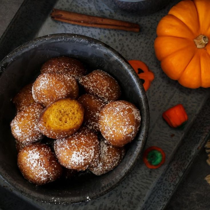 pumpkin fritters in a black bowl next to a small orange pumpkin - Easy Spanish Pumpkin Fritters