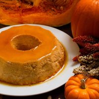 pumpkin spice flan on a white plate next to various-sized pumpkins and a dry flower bouquet.
