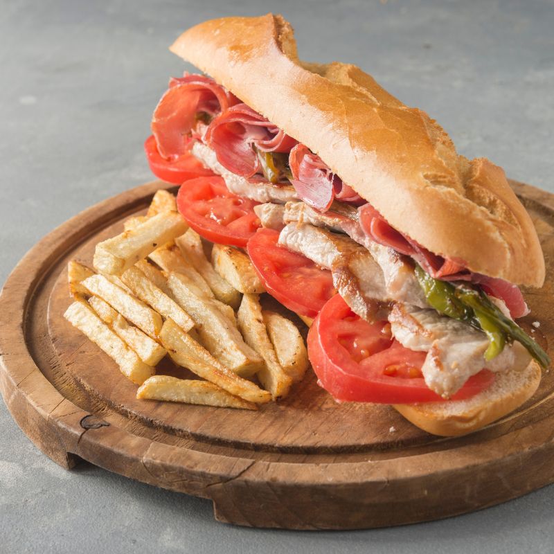 spanish sandwich with steak and tomato, and fries on a wooden plate.