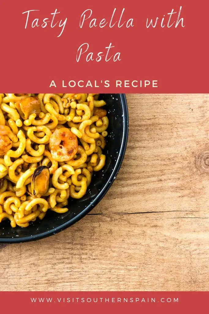 A bowl of paella with pasta and seafood on a wooden table. On top it's written tasty paella with pasta.