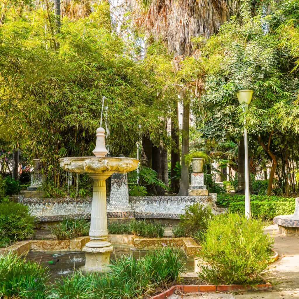 a garden with a fountain in the middle surrounded by trees